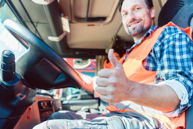 Truck driver sitting in cabin giving thumbs-up